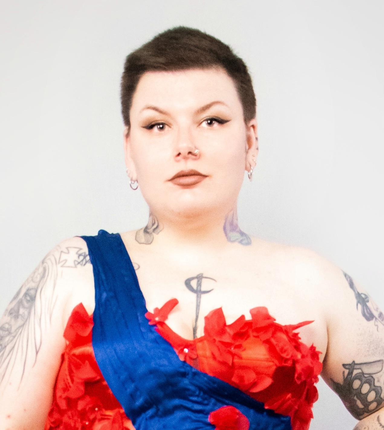 L’image montre Elisa dans le cadre d’une campagne du collectif SkinPower. Elle porte une robe rouge et une écharpe bleue, semblable à celles portées lors des concours de type « miss ». Le fond est blanc ou très clair, et sa posture dégage confiance et dignité, évoquant celle d’une reine.